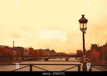 Paris en automne. Coucher de soleil. Le groupe de serrures d'amour est attaché à la lampe de rue. Vue sur la tour Eiffel, les ponts et les arbres dorés du parc de remblai. Photo en tons. Banque D'Images