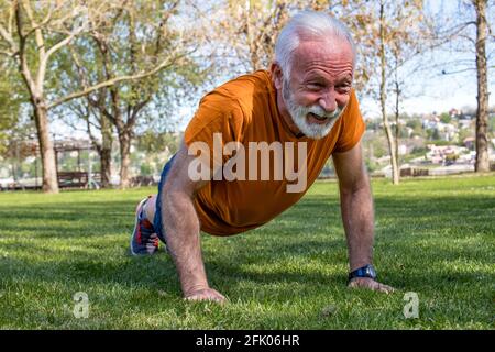 Portrait d'un homme âgé qui fait de l'exercice, qui fait des exercices dans le parc. Un homme âgé en bonne forme avec des bras forts. Banque D'Images