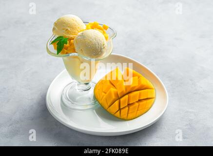 Crème glacée à la mangue avec menthe et mangue fraîche coupée en tranches sur fond gris. Vue latérale, espace de copie. Dessert sucré et frais à base de fruits et de crème. Banque D'Images