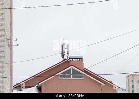 Antenne de télécommunication à côté d'un bâtiment résidentiel. Communications cellulaires et téléphoniques. Cheminée contre le ciel gris. Les fils électriques sont situés à différents endroits. Banque D'Images