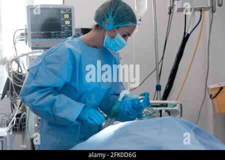 Femme de race blanche chirurgien portant un masque facial mettant le masque d'oxygène sur patient allongé dans le lit Banque D'Images