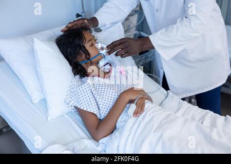 Section médiane d'un médecin de sexe masculin mettant le ventilateur de masque d'oxygène sur malade fille de race mixte dans le lit d'hôpital Banque D'Images