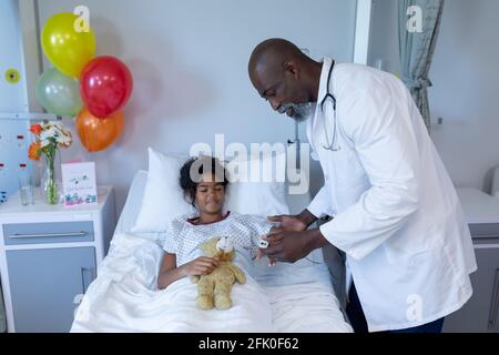 African american médecin mettant oxymètre de pouls sur malade mélangé fille de race dans le lit d'hôpital Banque D'Images