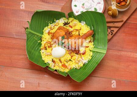 Poulet biryani , poulet de style kerala dhum biriyani fait à l'aide de riz de la jeera et des épices disposées sur une texture en bois avec rithaet citron pickle comme côté d Banque D'Images