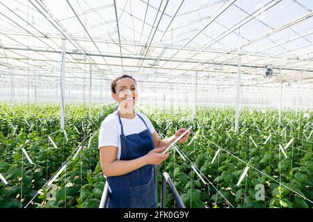 joyeux agriculteur afro-américain debout avec une tablette numérique dans un serre-tête Banque D'Images