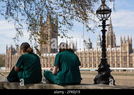 Londres, Royaume-Uni, 27 avril 2021 : les médecins étudiants Charlie et Surina prennent une pause au-dessus du mur commémoratif national Covid alors que le Premier ministre Boris Johnson est toujours accusé d'avoir préféré que les « corps s'accumulent » plutôt que d'avoir un troisième verrouillage. Avec un coeur dessiné pour chacun des plus de 150,000 personnes qui sont mortes dans la pandémie de coronavirus au Royaume-Uni, le mémorial s'étend le long du mur de l'hôpital St Thomas, en face du Parlement sur la rive opposée de la Tamise. Anna Watson/Alay Live News Banque D'Images