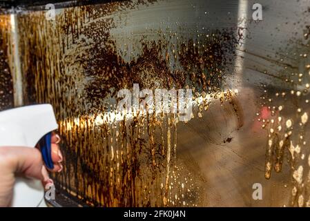 Une femme vaporisant un coin de verre couvert de suie dans une cheminée moderne avec une chambre de combustion fermée debout dans le salon. Banque D'Images