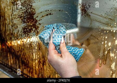 Une femme lave avec un tissu de cuisine la vitre d'angle couverte de suie d'une cheminée moderne avec une chambre de combustion fermée. Banque D'Images