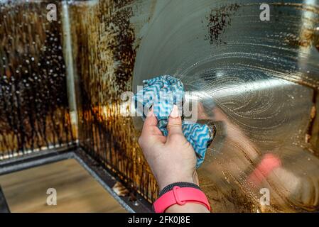 Une femme lave avec un tissu de cuisine la vitre d'angle couverte de suie d'une cheminée moderne avec une chambre de combustion fermée. Banque D'Images