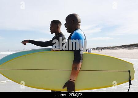Père et fils afro-américains avec planches de surf marchant vers le vagues à la plage Banque D'Images