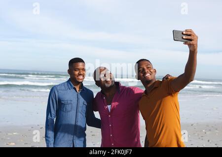 Père afro-américain et ses deux fils prenant un selfie depuis un smartphone à la plage Banque D'Images