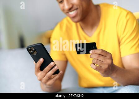 Une carte de crédit et un smartphone dans les mains des hommes. Joyeuse course mixte jeune homme dans defocus utilise le téléphone mobile et la carte de crédit pour le paiement en ligne, saisir les détails de la carte, les commandes à domicile livraison. Achats en ligne Banque D'Images