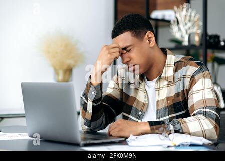 Fatigué épuisé course mixte réussie latino homme indépendant ou employé de bureau, assis au bureau avec les yeux fermés, se frotte ses yeux, sensation de mal de tête, le stress et la fatigue du travail supplémentaire, besoin de repos Banque D'Images