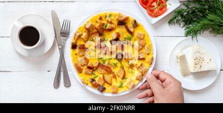 Omelette avec morceaux de pain grillé, fromage de chèvre et une tasse de café. Petit déjeuner délicieux et nourrissant. Main mâle prend une plaque, vue de dessus. Bannière Banque D'Images