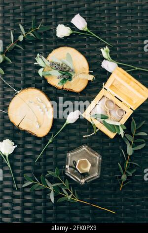 Les anneaux de mariage se trouvent dans une boîte en bois entourée de fleurs et des brindilles avec des feuilles sur fond vert osier Banque D'Images