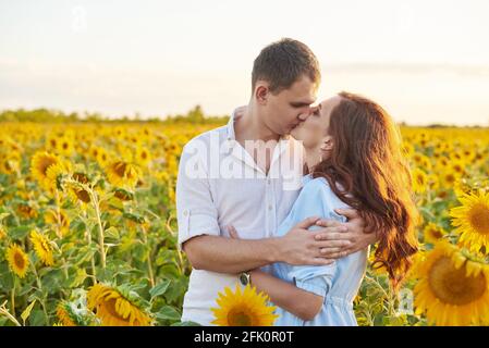 Sourire heureux couple embrassant au milieu d'un champ avec des tournesols. Reflet du soleil. Couple romantique sur un moment d'amour. Banque D'Images