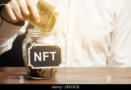 Main met des billets de dollars dans le pot de verre avec le mot NFT. Jeton non fongible. Produit ou ressource représenté numériquement. Vendre des ressources numériques et des œuvres d'art Banque D'Images
