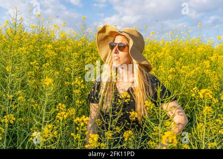 Femme en paille soleil chapeau appréciant le printemps dans le champ de fleurs jaunes. Banque D'Images