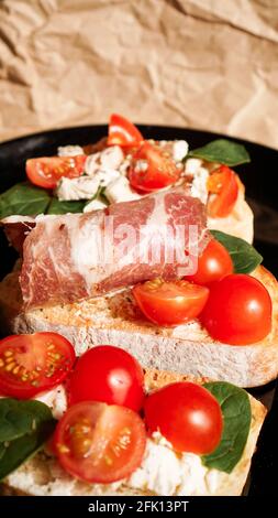 Trois bruschetta sur une assiette noire sur papier artisanal. Photo verticale Banque D'Images