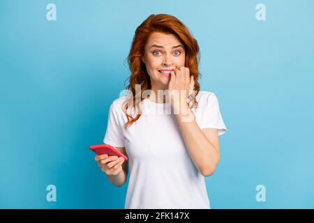 Photo portrait d'une femme mordant des ongles tenant le téléphone en un isolé à la main sur fond bleu pastel Banque D'Images