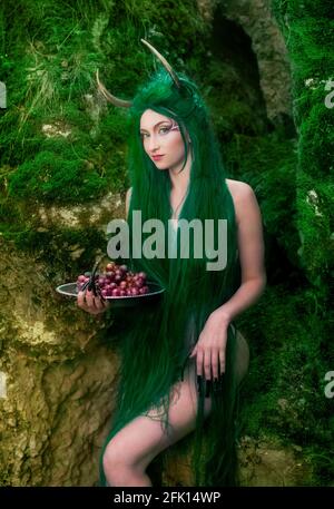 Signe mythique de l'horoscope du zodiaque Taurus. Belle fille mystère avec de longs cheveux verts et des cornes de cerf dans la forêt de printemps, heureux regardant l'appareil photo et le holdin Banque D'Images