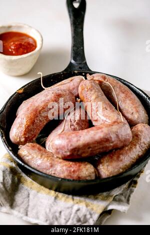 Saucisses italiennes grillées salsiccia dans une poêle en fonte sur une serviette en tissu sur une table en marbre blanc. Pose à plat, espace Banque D'Images