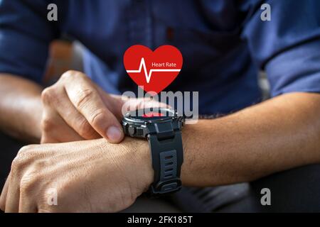 main de l'homme portant une montre intelligente affichant une icône de fréquence cardiaque avec une mise au point douce et une lumière excessive en arrière-plan. Banque D'Images