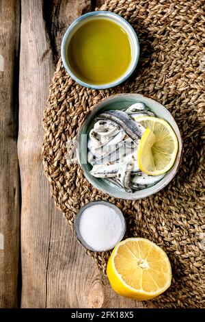 Bol d'anchois marinés ou filet de sardines dans l'huile, servi avec du citron, de l'huile d'olive, du sel pour tapas ou antipasti sur fond de bois ancien. Pose à plat, c Banque D'Images