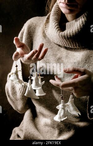 Anges de Noël en porcelaine. Femme en laine pull tenir les doigts ensemble de blanc artisanat fait main Noël anges décoration. Arrière-plan sombre. Banque D'Images