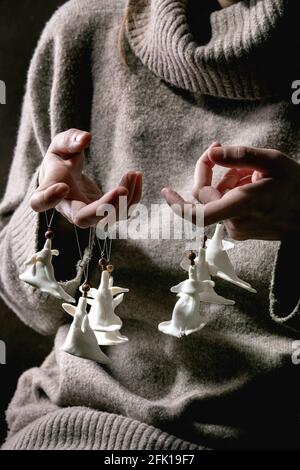 Anges de Noël en porcelaine. Femme en laine pull tenir les doigts ensemble de blanc artisanat fait main Noël anges décoration. Arrière-plan sombre. Banque D'Images