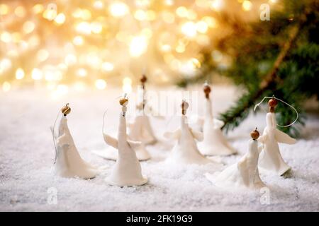 Anges de Noël en porcelaine. Ensemble de décorations artisanales de Noël faites à la main sur la neige avec des lumières de Noël bokeh et des branches de sapin. Banque D'Images