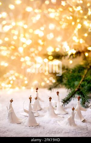 Anges de Noël en porcelaine. Ensemble de décorations artisanales de Noël faites à la main sur la neige avec des lumières de Noël bokeh et des branches de sapin. Banque D'Images