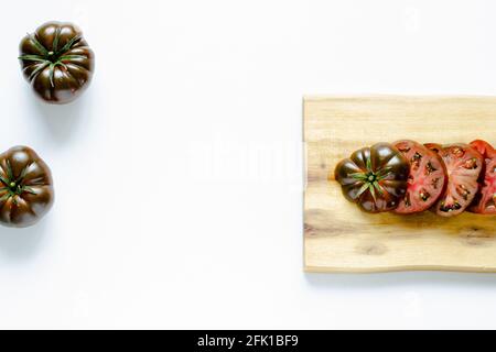 Couper et des tomates rouges entières sur une planche à découper en bois et arrière-plan blanc Banque D'Images