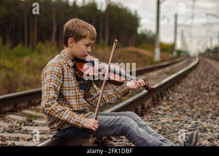 Un beau garçon blond est assis sur les rails du chemin de fer et joue le v Banque D'Images