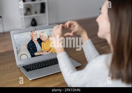 Réunion vidéo avec un grand-père sur l'ordinateur portable, un couple senior à l'écran, une petite-fille leur montre la forme du cœur en signe d'amour. Appel vidéo à la famille pendant une pandémie, réunion virtuelle Banque D'Images