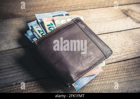 Certains billets en euros sortent d'UN portefeuille en cuir marron Sur UNE planche en bois avec un angle de vue élevé Banque D'Images