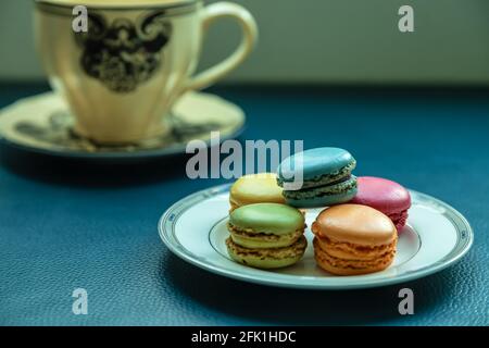 macarons colorés sur une assiette, avec théière en arrière-plan. Banque D'Images