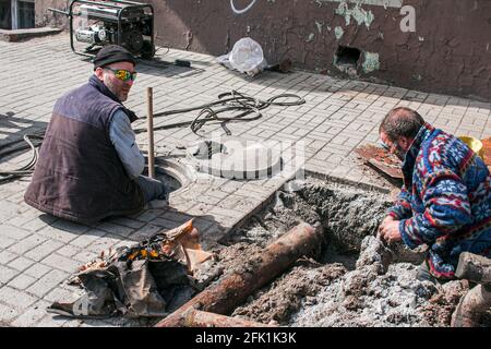 Dnepropetrovsk, Ukraine - 03.26.2021: Les travailleurs des services de distribution d'eau ouvrent un ancien trou d'homme et remplacent les vieux tuyaux rouillés par de nouveaux. Banque D'Images