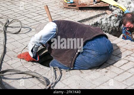Dnepropetrovsk, Ukraine - 03.26.2021: Les travailleurs des services de distribution d'eau ouvrent un ancien trou d'homme et remplacent les vieux tuyaux rouillés par de nouveaux. Banque D'Images