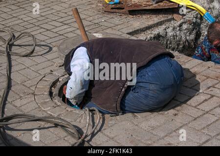 Dnepropetrovsk, Ukraine - 03.26.2021: Les travailleurs des services de distribution d'eau ouvrent un ancien trou d'homme et remplacent les vieux tuyaux rouillés par de nouveaux. Banque D'Images