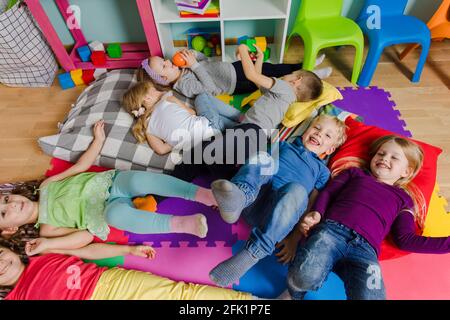 Les enfants actifs s'assetent sur des oreillers et des tapis moelleux à la maternelle Banque D'Images