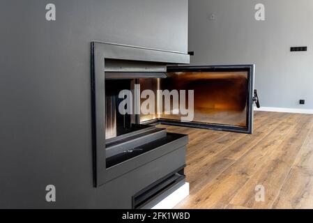 Panneau d'angle ouvert et sale dans une cheminée moderne avec une chambre de combustion fermée dans la salle de séjour, peinte en noir. Banque D'Images