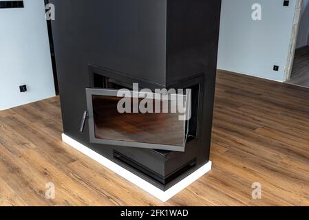 Panneau d'angle ouvert et sale dans une cheminée moderne avec une chambre de combustion fermée dans la salle de séjour, peinte en noir. Banque D'Images