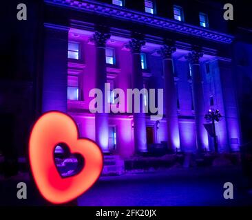 Bâtiment du patrimoine avec colonnes et fenêtres illuminées la nuit avec des lumières pourpres et roses avec un grand coeur changeant de couleur sur le trottoir Banque D'Images