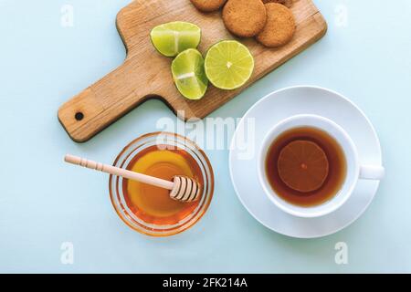 Une tasse de thé et de miel dans un bol en verre avec un pot en bois, de la chaux et des biscuits sur le plan de coupe sur fond bleu. Petit déjeuner sain. Vue de dessus, plan d'appartement. Banque D'Images
