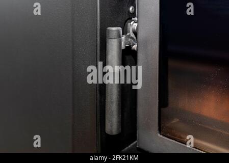 Une poignée et une fermeture dans une cheminée moderne avec une chambre de combustion fermée debout dans le salon en noir. Banque D'Images