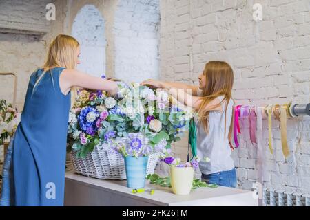 Deux fleuristes femmes font un grand panier fleuri avec des fleurs dans la chambre lumineuse Banque D'Images