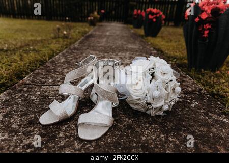 Mise au point sélective d'une paire de chaussures de mariage avec un bouquet blanc dans le jardin Banque D'Images