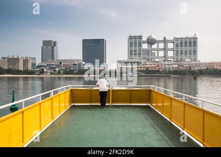 Seul homme japonais sur le bateau. Odaiba ferry avec l'île d'Odaiba et Aqua City au loin. Tokyo, Japon Banque D'Images