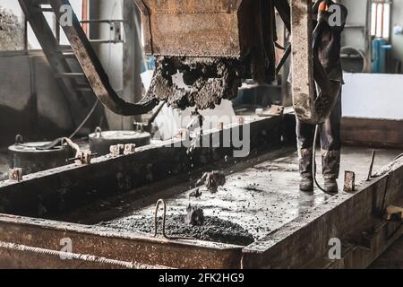 Un travailleur de la construction contrôle le flux de béton et de gravier à partir d'un mélangeur dans un atelier de barres d'armature d'une usine industrielle, foyer sélectif. Banque D'Images